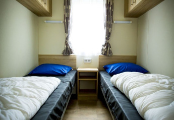 Small twin bedroom with two single beds, window and wooden cabinets at Forest Lodge, Holiday Park Duinhoeve.