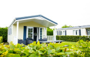 Delta Lodge op Holiday Park Duinhoeve in Nederland, met tuinmeubilair op het terras en groene heggen.