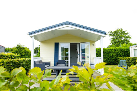 Delta Lodge at Holiday Park Duinhoeve in the Netherlands, featuring a covered porch, outdoor seating and greenery.