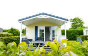 Delta Lodge bij Holiday Park Duinhoeve in Nederland, met overdekte veranda, loungestoelen en groene heggen.