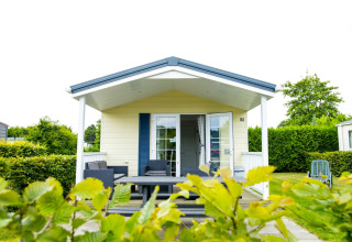 Delta Lodge en Holiday Park Duinhoeve, Países Bajos, con porche cubierto, asientos y exuberante vegetación.