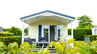 Delta Lodge im Holiday Park Duinhoeve, Niederlande, mit überdachter Veranda, Sitzmöbeln und gepflegtem Garten.