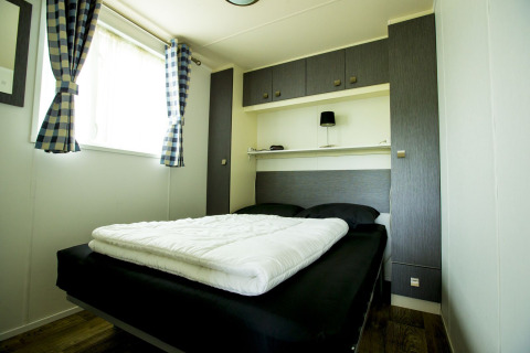 Habitación moderna con cama doble y cortinas a cuadros en Delta Lodge, Holiday Park Duinhoeve, Países Bajos.