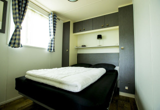 Habitación moderna con cama doble y cortinas a cuadros en Delta Lodge, Holiday Park Duinhoeve, Países Bajos.