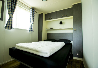 Camera moderna con letto matrimoniale e tende a quadri a Delta Lodge, Holiday Park Duinhoeve, Paesi Bassi.
