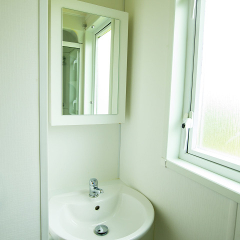 Salle de bain lumineuse avec lavabo blanc, miroir et fenêtre au Delta Lodge, Holiday Park Duinhoeve, Pays-Bas.