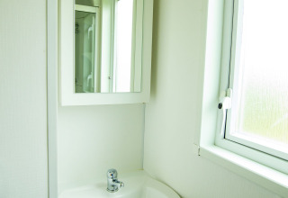 Lichte badkamer met witte wastafel, spiegel en raam in Delta Lodge, Holiday Park Duinhoeve, Nederland.