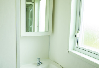 Baño luminoso con lavabo blanco, espejo y ventana en Delta Lodge, Holiday Park Duinhoeve, Países Bajos.