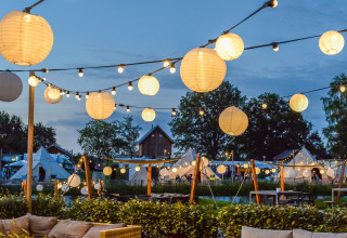 Evening view of Happy Harbor tent and bathroom at Holiday Park Mölke, Netherlands, with lantern lights.