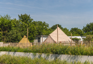 Tienda tipi con baño en Holiday Park Mölke, Países Bajos, rodeada de flores y vegetación.