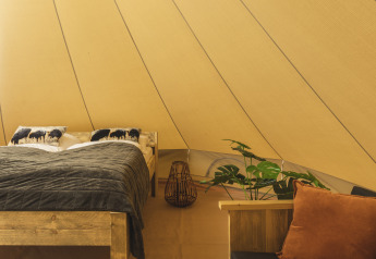 Gemütliches Bett mit Pflanzen und Kissen in einem Tipi-Zelt, mit warmen Stoff- und Holzakzenten.