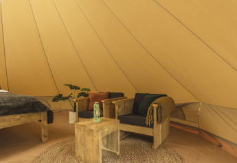 Innenraum eines Tipi-Zeltes mit Holzmöbeln, schwarzen Kissen, Laterne und gemütlichem Ambiente.