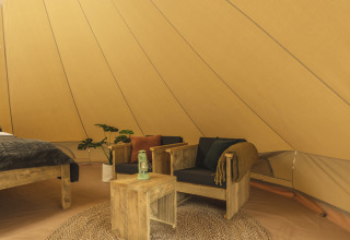 Interno di una tenda tipi con mobili in legno, cuscini neri, lanterna verde e atmosfera accogliente.