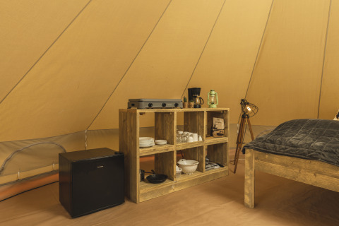 Interno di una tenda tipi con scaffale in legno, mini frigo, fornello e luci accoglienti.