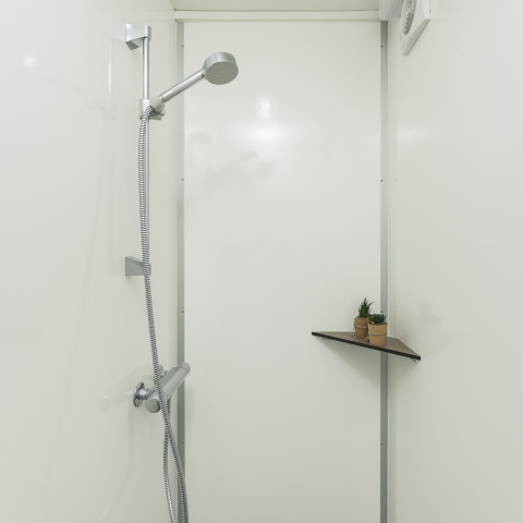 Een douche in een tipitent met een moderne zilveren douchekop en een hoekplankje met plantjes.