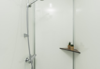 Een douche in een tipitent met een moderne zilveren douchekop en een hoekplankje met plantjes.