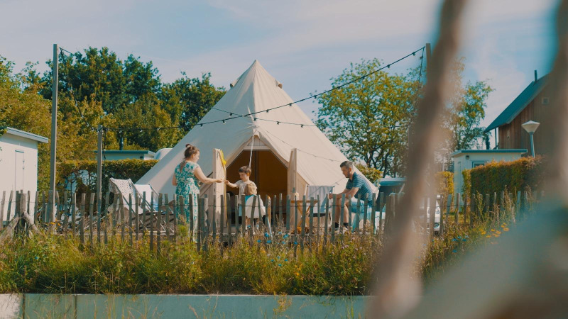 Gezin voor de Happy harbor tent met badkamer bij Holiday Park Mölke in Nederland op een zonnige dag.