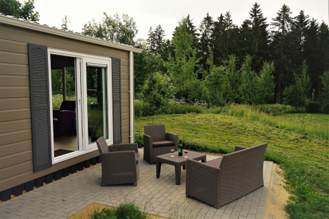 Terraza exterior del Chalet Brilon con muebles de jardín, césped y bosque en Camping Brilon, Alemania.