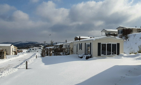 Cabañas cubiertas de nieve en Chalet Brilon, Camping & Ferienpark Brilon, Alemania, con cielo nublado.