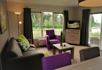 Salón en Chalet Brilon de Camping & Ferienpark Brilon, Alemania, con sofá, sillones y grandes ventanales.