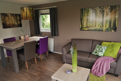 Sala en Chalet Brilon, Camping & Ferienpark Brilon, con decoración moderna y cuadros de bosque en las paredes.