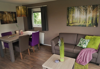 Sala en Chalet Brilon, Camping & Ferienpark Brilon, con decoración moderna y cuadros de bosque en las paredes.