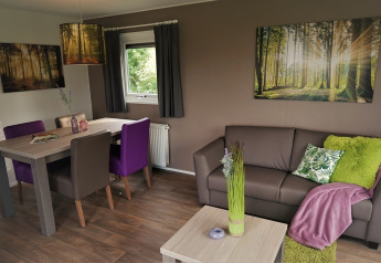 Sala en Chalet Brilon, Camping & Ferienpark Brilon, con decoración moderna y cuadros de bosque en las paredes.