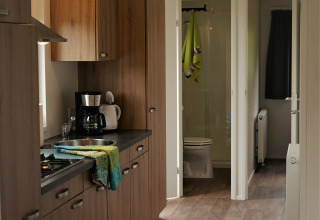 Cocina moderna de madera con cafetera y vista al baño en Chalet Brilon, Camping Brilon, Alemania.