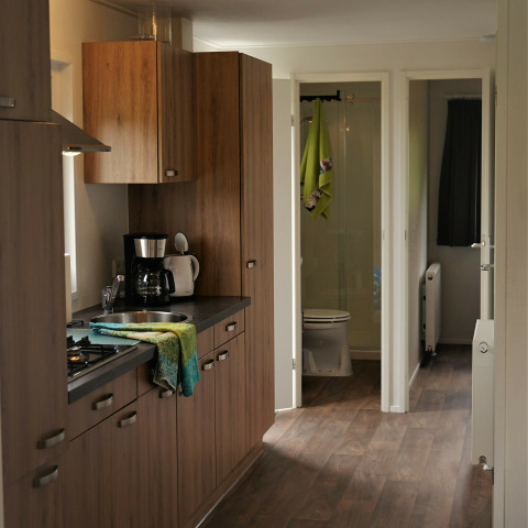 Cocina moderna de madera con cafetera y vista al baño en Chalet Brilon, Camping Brilon, Alemania.
