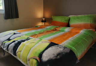 Cama doble con ropa de cama colorida en verde y naranja en Chalet Brilon, Camping & Ferienpark Brilon.