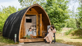 Eine Frau und ein Kind entspannen sich vor einer gemütlichen hölzernen Lodge im Kampeerdorp de Zandstuve.