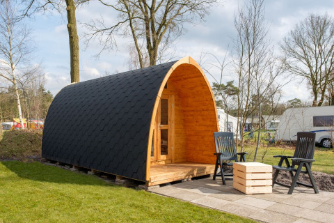 Trekkerpod-lodge ved Kampeerdorp de Zandstuve, Holland, med buet træhytte og udendørs siddepladser.