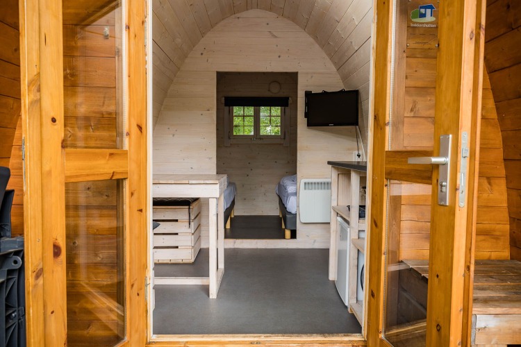 Vista interior de una cabaña Trekkerspod en Kampeerdorp de Zandstuve, Países Bajos, con camas y televisor.