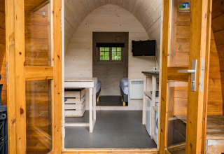 Vista interior de una cabaña Trekkerspod en Kampeerdorp de Zandstuve, Países Bajos, con camas y televisor.