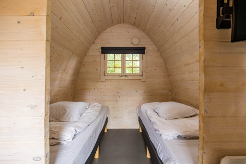 Trekkerspod-lodge interieur met twee eenpersoonsbedden en houten panelen in Kampeerdorp de Zandstuve.