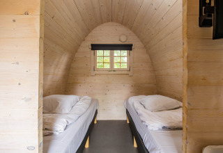 Intérieur du lodge Trekkerspod avec deux lits simples et panneaux de bois à Kampeerdorp de Zandstuve, Pays-Bas.