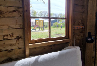 Vista desde la ventana de una cabaña de madera hacia un parque infantil. Foto en Writers hut, Zomerlicht, NL.