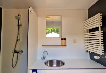 Moderne badkamer in een glampingaccommodatie met douche, wastafel, spiegel en wandhanddoekdroger.