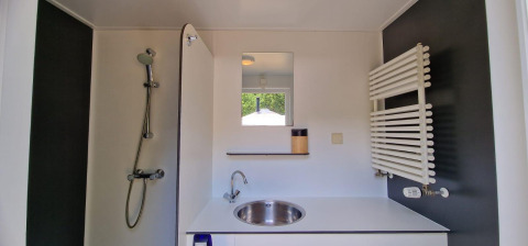 Baño moderno en alojamiento glamping con ducha, lavabo, espejo y radiador toallero en la pared.