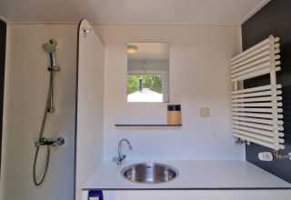 Bagno moderno in una struttura glamping con doccia, lavandino, specchio e scaldasalviette a parete.
