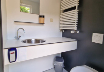 Bagno moderno da glamping con lavandino circolare, WC, specchio e termosifone minimalista.