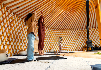 Des personnes pratiquant le yoga dans une yourte glamping luxueuse à la décoration chaleureuse en bois.