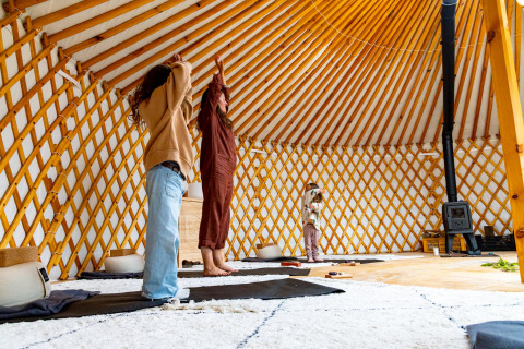 Mensen beoefenen yoga in een sfeervolle glamping yurttent met houten structuur en warm interieur.