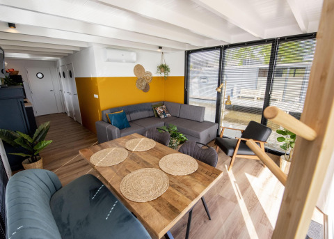 Sala y comedor del barco casa 'De Waterparel' con decoración moderna y grandes ventanas en Friesland, Países Bajos.