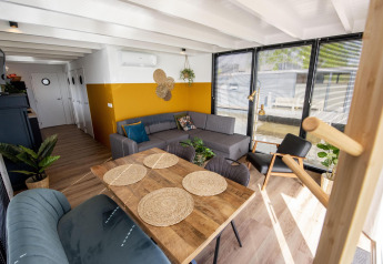 Sala y comedor del barco casa 'De Waterparel' con decoración moderna y grandes ventanas en Friesland, Países Bajos.