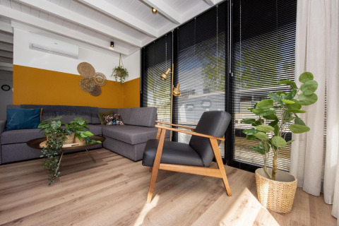 Moderne stue på husbåd 'De Waterparel' med grå sofa, sorte persienner og grønne planter i Friesland.