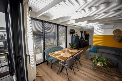 Soggiorno moderno sulla houseboat 'De Waterparel' in Frisia con ampie finestre e zona pranzo accogliente.