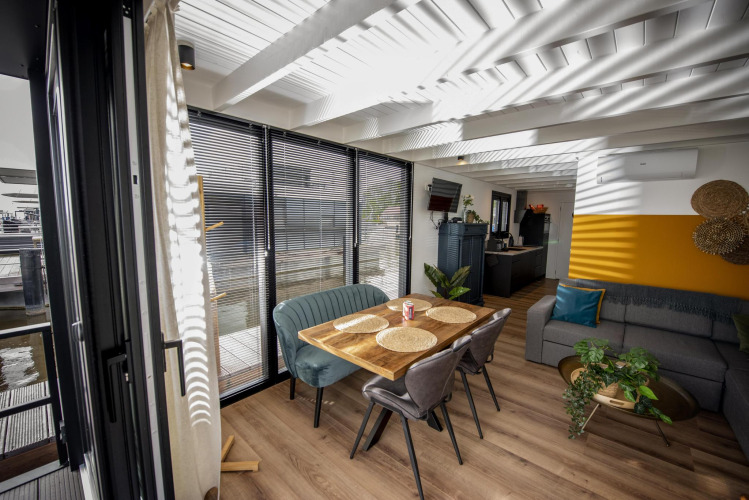 Modern living and dining area on Houseboat 'De Waterparel' in Friesland, with large windows and wood decor.