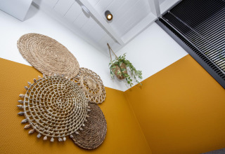 Originele wanddecoratie en een hangplant in een trendy hoekje met mosterdmuur op een woonboot in Friesland.