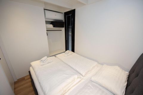 Chambre moderne à bord de la péniche 'De Waterparel' à Welcome In - Friesland, aux Pays-Bas, avec lit et placard ouvert.